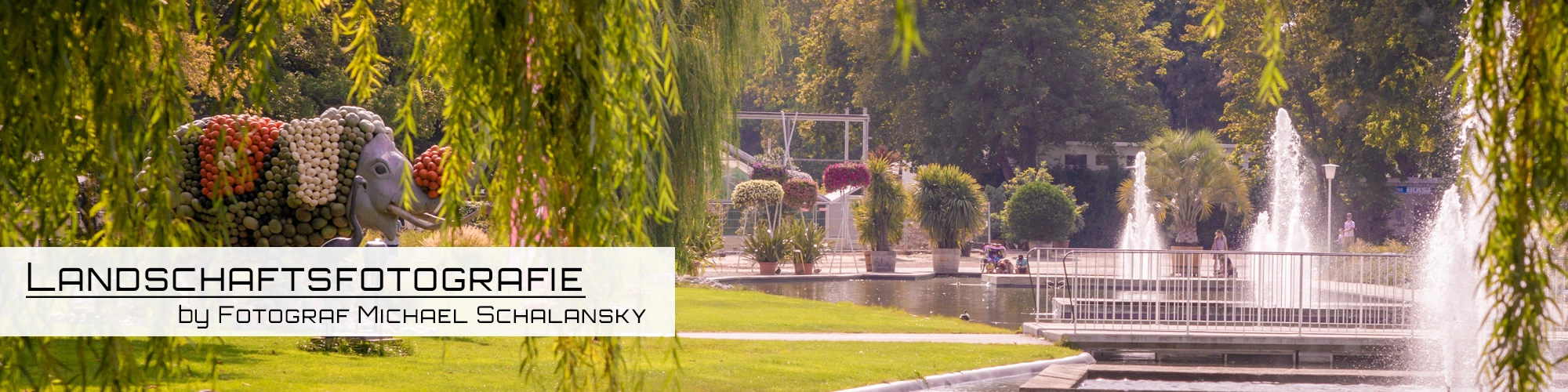 Michael Schalanskys ästhetische Darstellung des EGA-Parks Erfurt, fokussiert auf die einzigartige Pflanzenskulptur eines Elefanten und die Wasserspiele, die in einem lebendigen grünen Ambiente eingebettet sind.